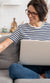 Person wearing glasses while sitting on a couch, legs crossed with a laptop.