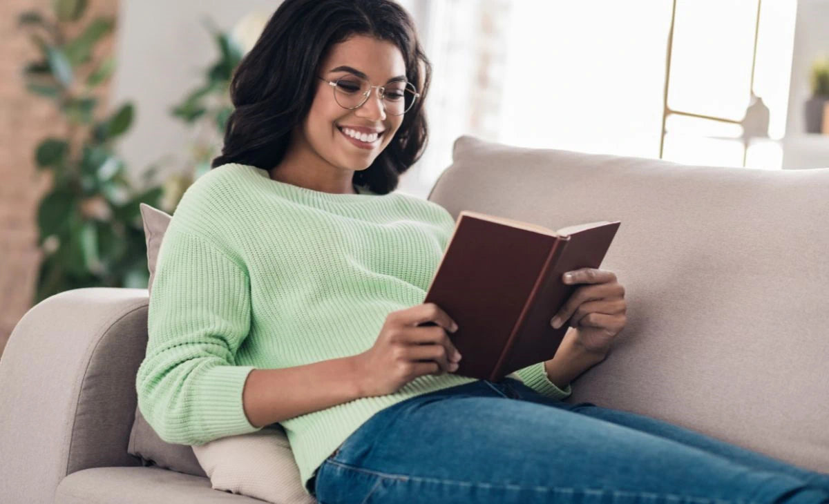 Women laying on couch reading a book wearing a pair of ICU Eyewear reading glasses.